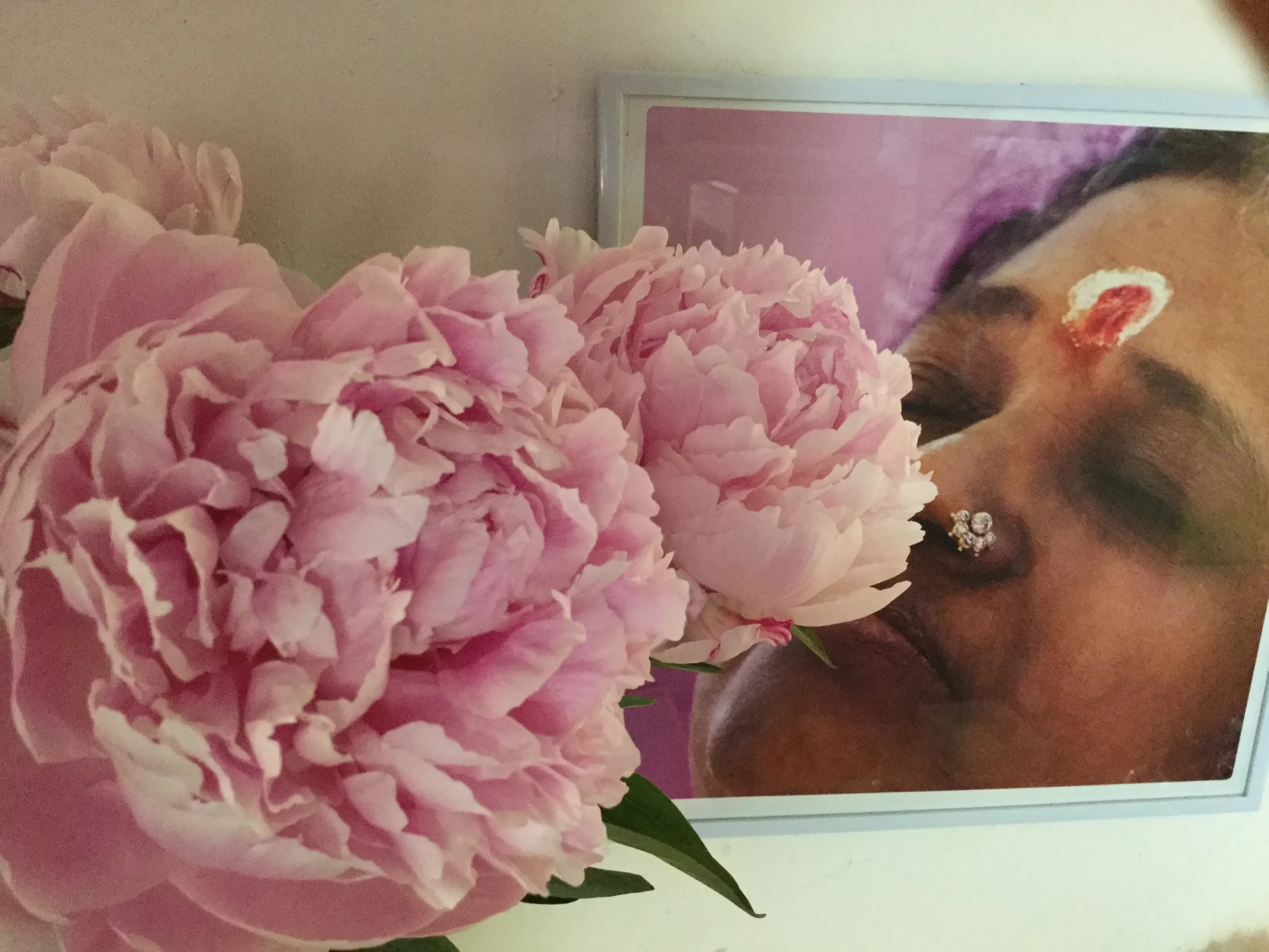 Pivoines roses en premier plan devant une photo d'Amma souvenir de pèlerinage en Inde, douceur et soin dans le Var.