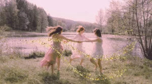 Ronde de femmes dansant au bord d'un lac avec effet d'énergie dorée, sororité et soin dans le Var lors d'un pèlerinage.