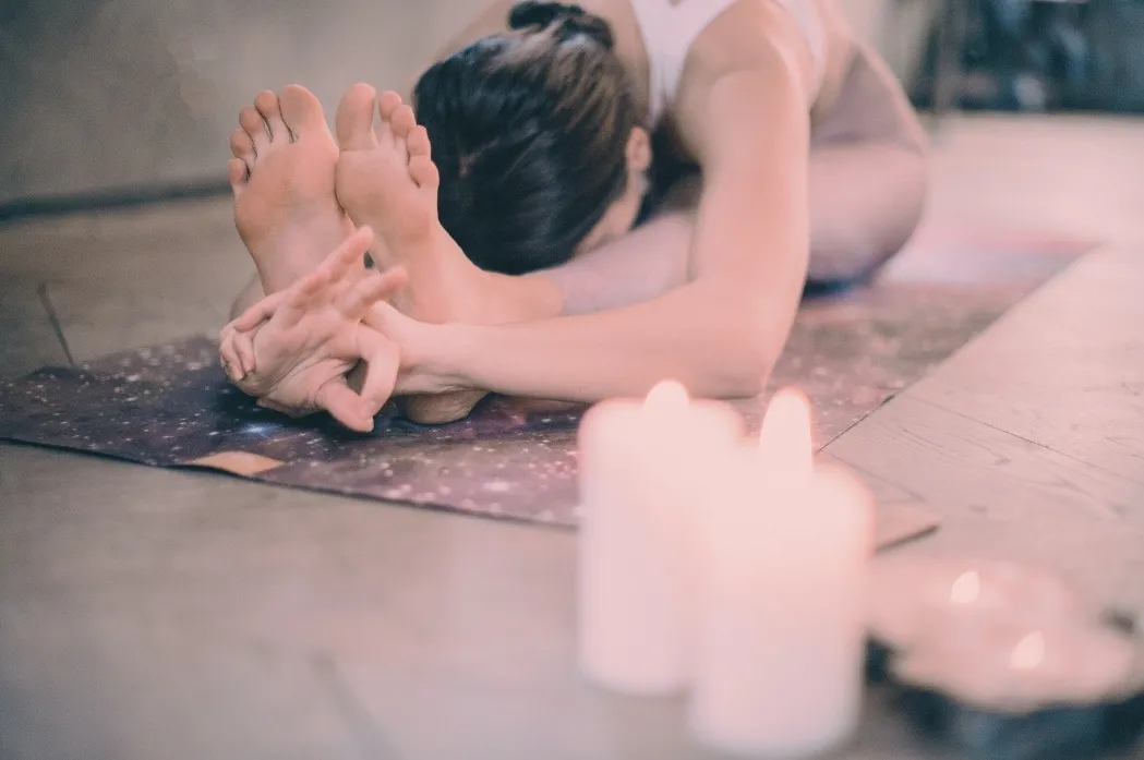 Femme réalisant un étirement intense en cours de yogathérapie dans une ambiance zen avec bougies près de Draguignan, Var.