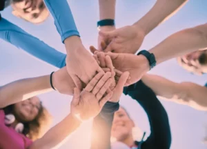 Groupe de jeunes empilant leurs mains au centre en cercle lors d'un atelier collectif de yogathérapie à Vidauban, Var.
