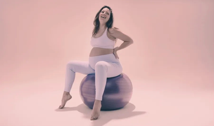 Femme enceinte souriante pratiquant la yogathérapie prénatale sur un ballon de gym pour soulager le dos à Lorgues, Var.